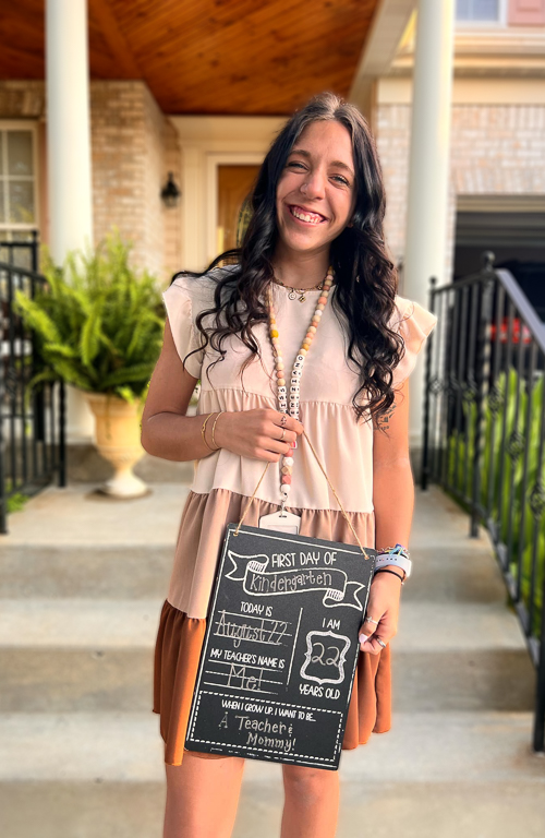School of Education alum Caterina Veneziano with first day of school sign outside with home in background.