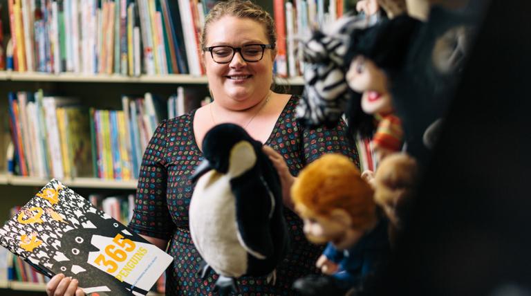 Photo of School of Education teacher in curriculum center with puppets in foreground and bookshelves in background