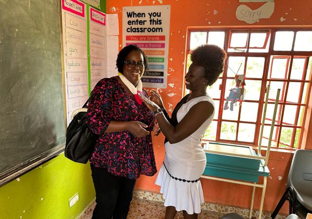 Dr. Rachel Ayieko smiling and conversing colleague in classroom with learning materials on colorful walls and chalkboard in background at Jaramongi Oginga Odinga University of Science and Technology in Kenya