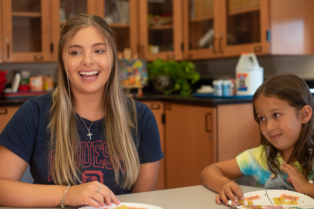 Duquesne student teacher engaging in lesson at table with K-12 student next to her in clasroom with paper plate science project.