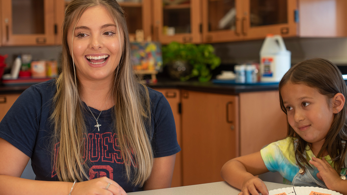 Duquesne student teacher engaging in lesson at table with K-12 student next to her in clasroom with paper plate science project.