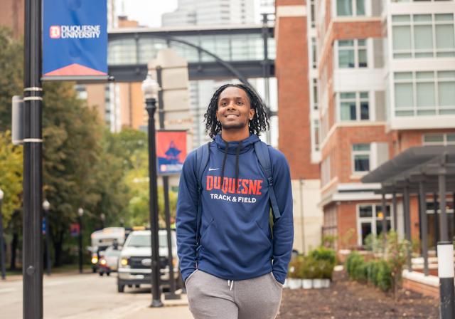 Duquesne University student walking with confidence on Forbes Avenue in Duquesne hoodie