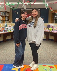 Early Childhood Education student Kenzie Boland with student colleague in decorated and colorful library smiling in colleague embrace