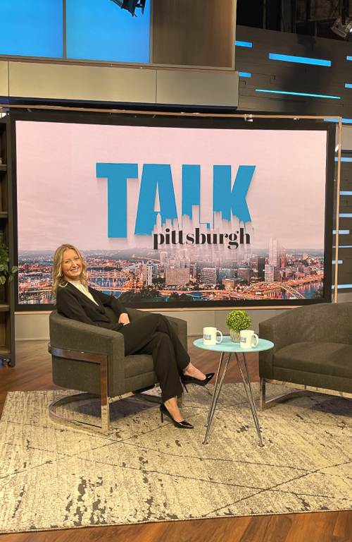 Education alum Maggie Burke seated and smiling on KDKA studios set for Pittsburgh Talk with the show signage behind her.