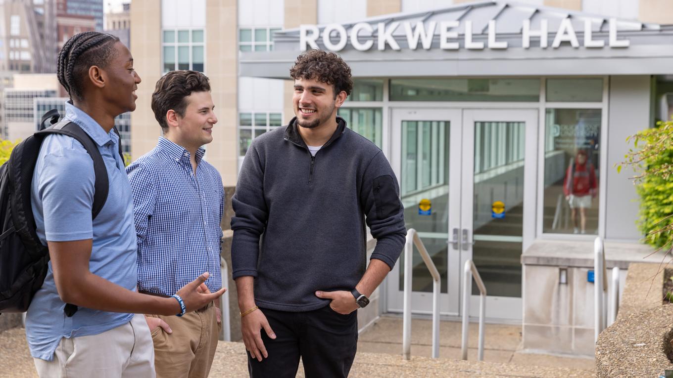 Three students chat outside of Rockwell Hall's entrance. 