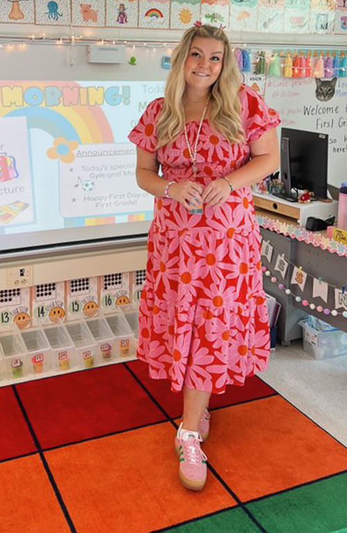 School of Education alum Alexa Nye stands in 1st grade classroom in front of board.